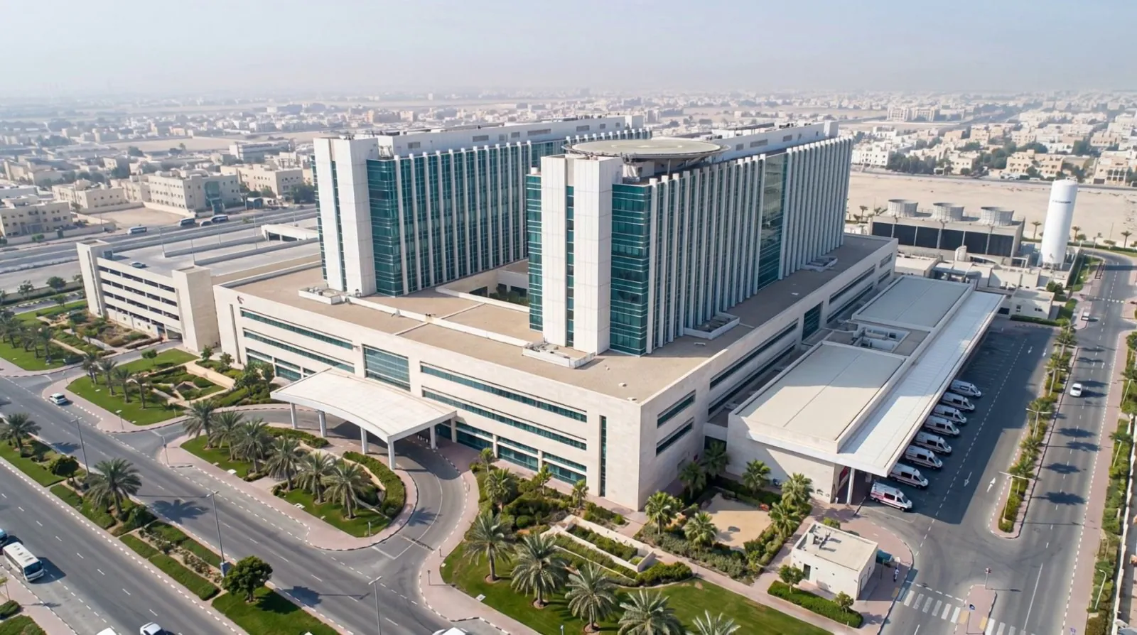 Aerial view of a desert hospital campus with two ward towers, a rooftop helipad, the podium entrance and an ambulance bay.